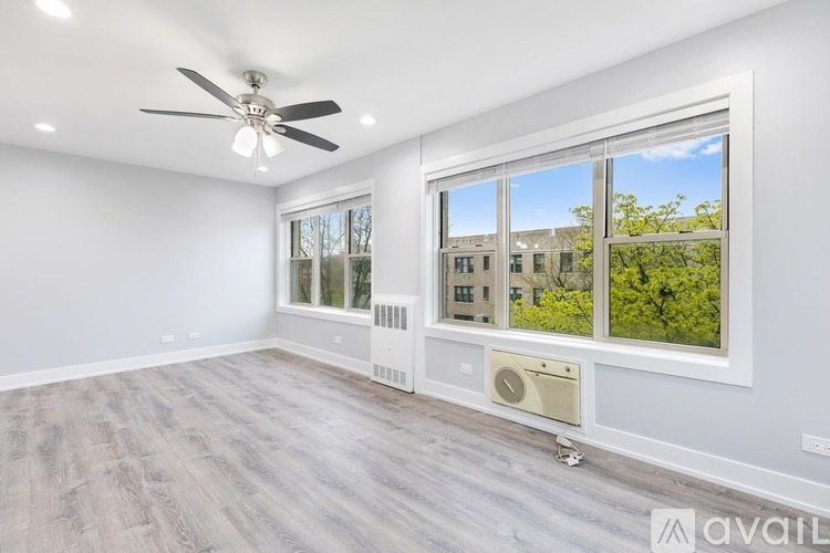 A spacious room with a ceiling fan, large windows, and a heating and cooling unit on the floor.