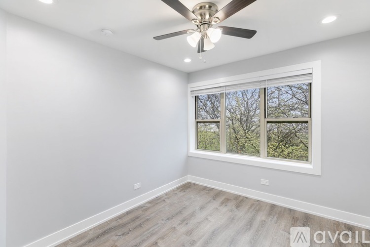 A room with a ceiling fan and a window showing trees outside.