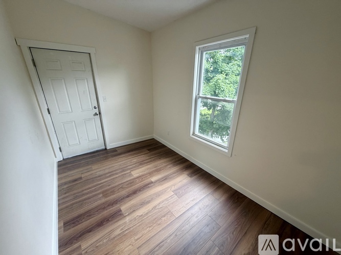 A room with a white door and a window with a view of trees.