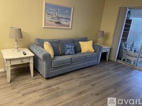 A living room with a grey couch, a small table with a lamp, and a painting on the wall.