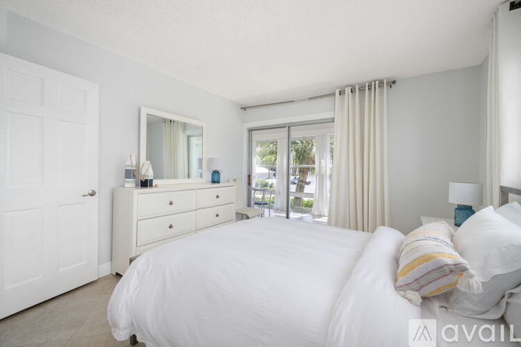 A bedroom with a large bed, a dresser with a mirror, and a sliding glass door leading to a balcony.