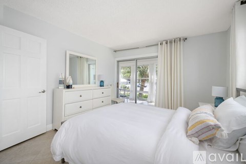 A bedroom with a large bed, a dresser with a mirror, and a sliding glass door leading to a balcony.
