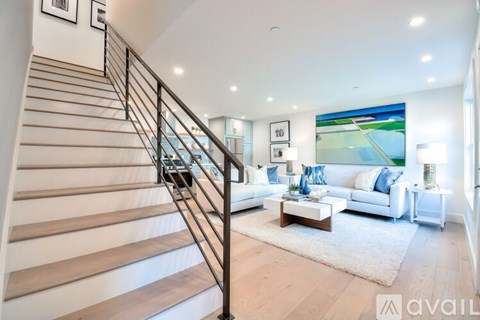 A staircase with a metal railing leads to a brightly lit living room with a white couch and a coffee table.