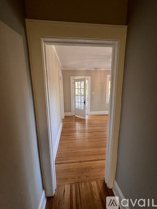 A hallway with wooden floors and white walls leading to a bright room.