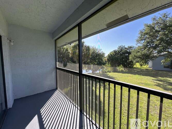 A balcony with a black railing and a view of a green lawn and trees.