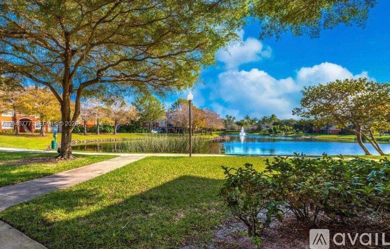 A park with a lake, trees, and a clear sky.