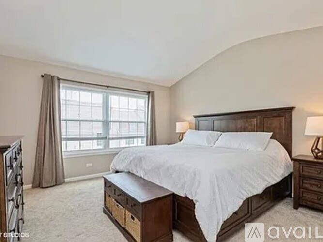 A bedroom with a large bed and a window with curtains.