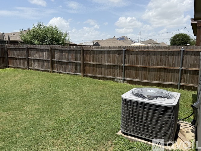 A large air conditioner unit sits on a grassy lawn in front of a wooden fence.