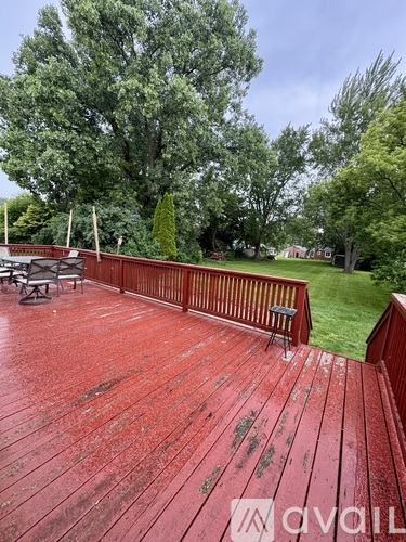 A red wooden deck with a bench and trees in the background.