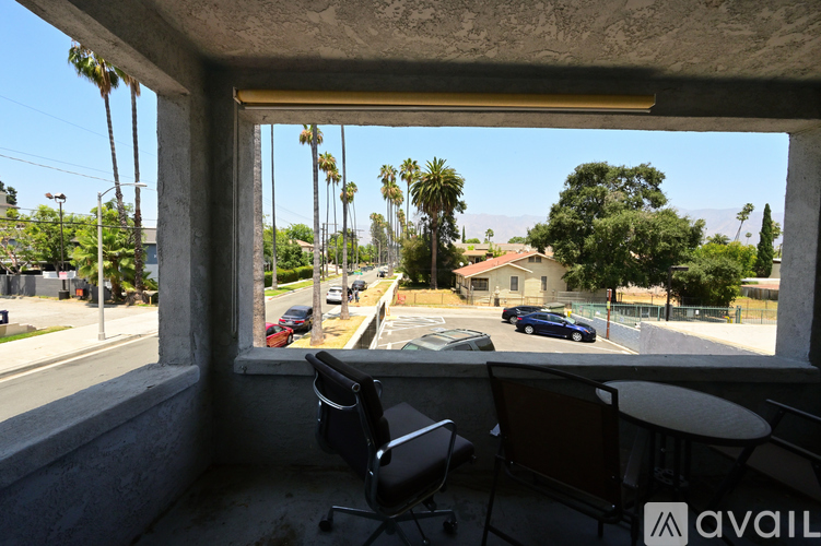 A balcony with chairs and a table overlooks a street with cars and palm trees.