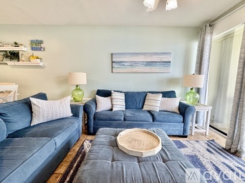 A living room with blue couches and a painting on the wall.