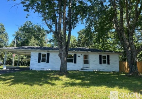 A white house with black shutters is surrounded by trees.