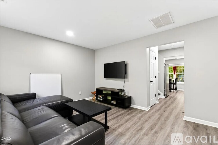 A black leather couch sits in a living room with a television and a whiteboard on the wall.