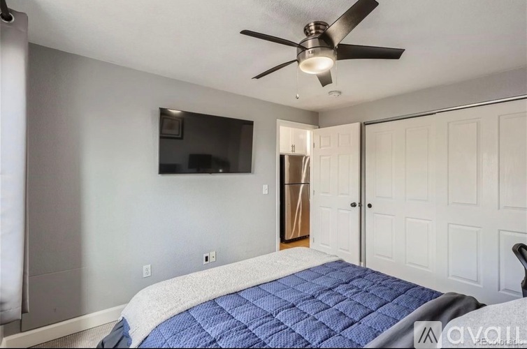 A bedroom with a bed, a ceiling fan, and a television mounted on the wall.