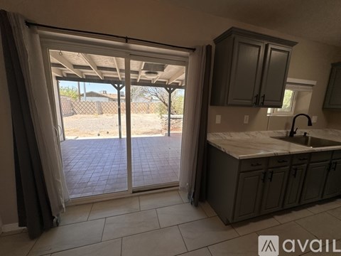 A kitchen with a sink and cabinets under a window with a view of a backyard.