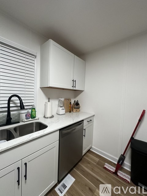 A kitchen with white cabinets and a black trash can.