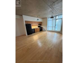 A spacious room with wooden floors and a kitchen area with black appliances.