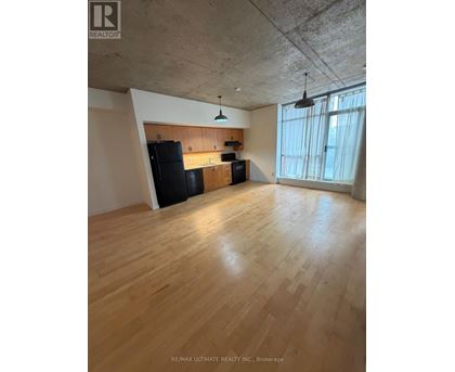 A spacious room with wooden floors and a kitchen area with black appliances.