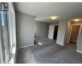 A spacious room with grey carpeting and white walls, with a door leading to another room visible in the background.