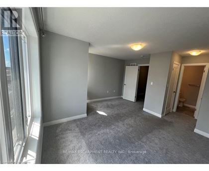 A spacious room with grey carpeting and white walls, with a door leading to another room visible in the background.