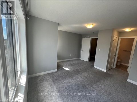 A spacious room with grey carpeting and white walls, with a door leading to another room visible in the background.