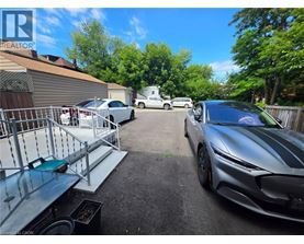 A silver sports car is parked in a driveway with a metal grill and a green bench.