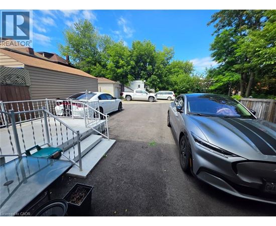 A silver sports car is parked in a driveway with a metal grill and a green bench.