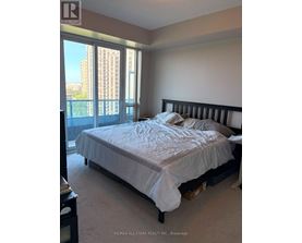 A bedroom with a large bed and a view of a city skyline through the windows.