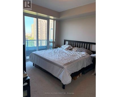 A bedroom with a large bed and a view of a city skyline through the windows.