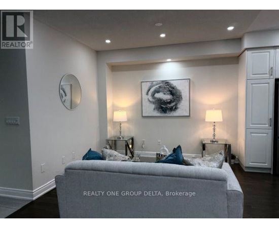 A living room with a grey couch and a painting on the wall.