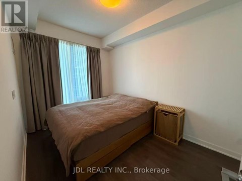 A bedroom with a bed, a window with curtains, and a wooden crate on the floor.