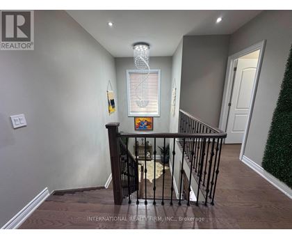 A hallway with a chandelier, a framed picture on the wall, and a staircase with a railing.