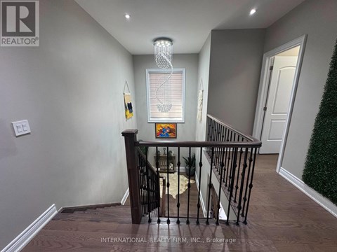 A hallway with a chandelier, a framed picture on the wall, and a staircase with a railing.