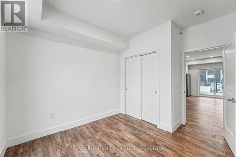 A room with white walls and wooden flooring, with a door on the right side.