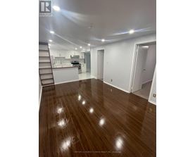 A spacious room with wooden flooring and a staircase leading to the upper level.
