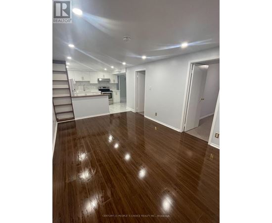 A spacious room with wooden flooring and a staircase leading to the upper level.