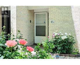 A white door with the number 85 on it is flanked by pink and white flowers.