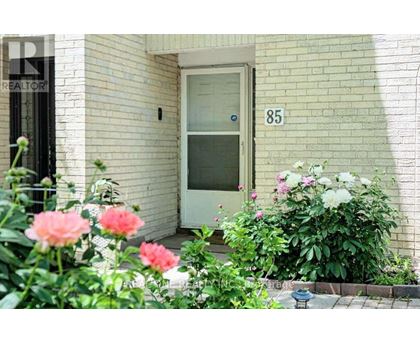 A white door with the number 85 on it is flanked by pink and white flowers.