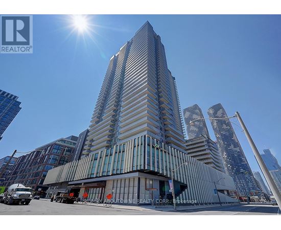 A tall building with a glass facade stands in the foreground with the sun shining brightly in the sky.