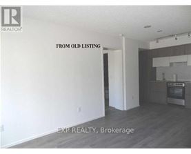 A room with a kitchen area in the background and a doorway leading to another room.