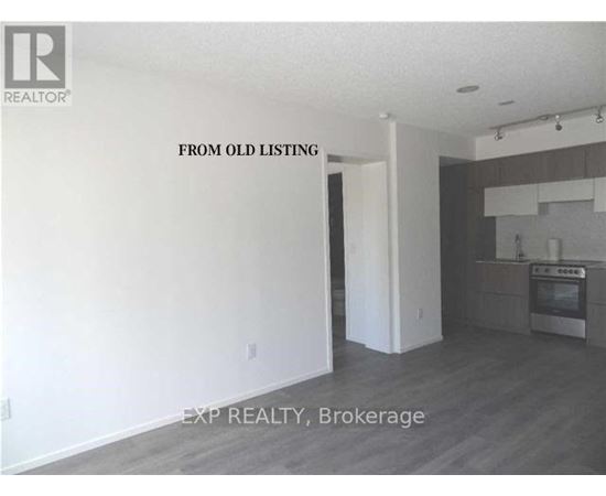 A room with a kitchen area in the background and a doorway leading to another room.