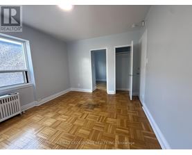 A room with wooden flooring and white walls, with a window on the left side.