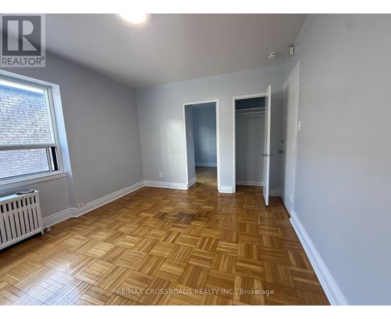 A room with wooden flooring and white walls, with a window on the left side.