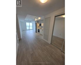 A spacious room with wooden flooring and a kitchen area with white appliances.