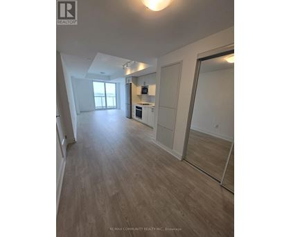 A spacious room with wooden flooring and a kitchen area with white appliances.