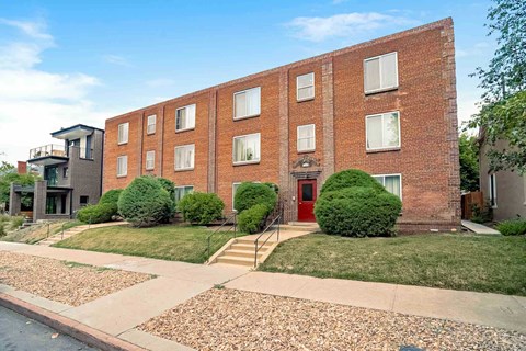 A red brick building with a red door and a small balcony on the second floor.