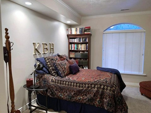 A bedroom with a bed, a bookshelf, and a window with blinds.