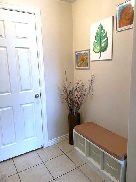 A white door is on the left of a hallway with a bench and pictures on the wall.