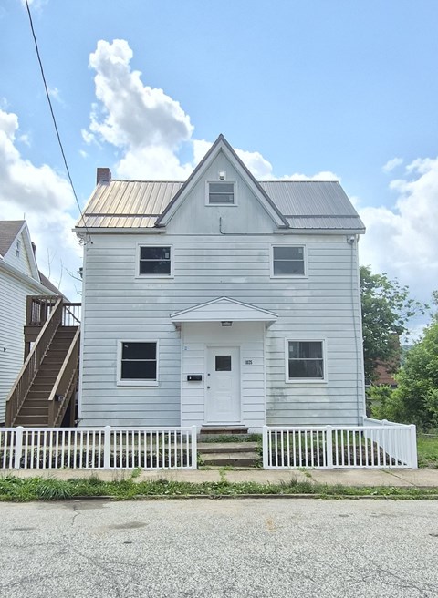 A white house with a grey roof and a white fence in front.