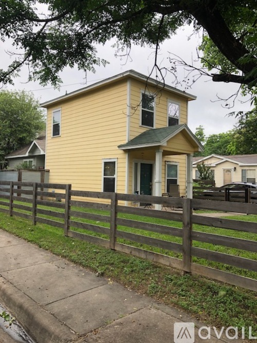 A yellow house with a green roof and a wooden fence in front.